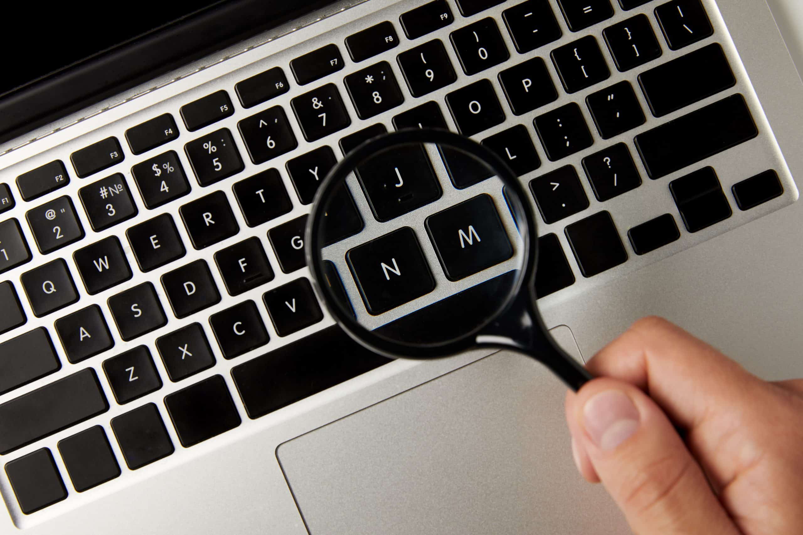 Person holding magnifying glass over laptop